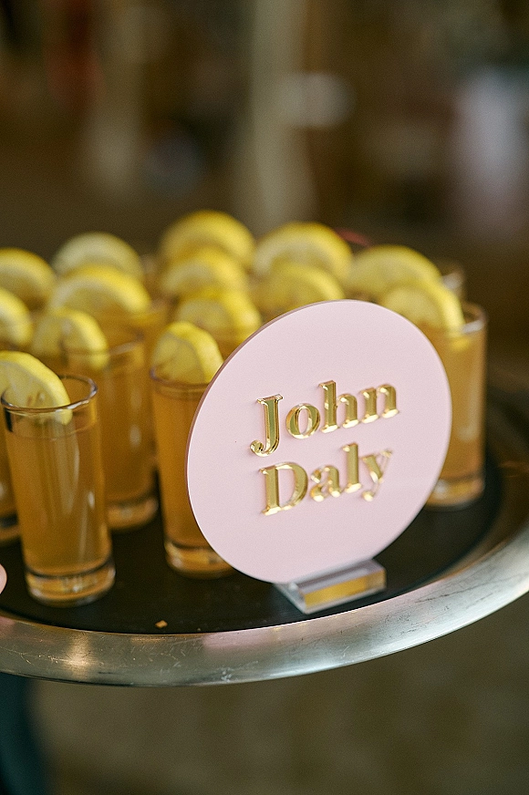 Wedding drink display with signature drink table sign, cocktail glasses and lemon wedges on a tray in a softly blurred indoor bar area