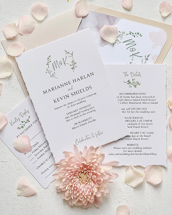 Wedding invitation suite with deckle edge wedding invitations, blush envelope and greenery monogram on a white textured surface with rose petals