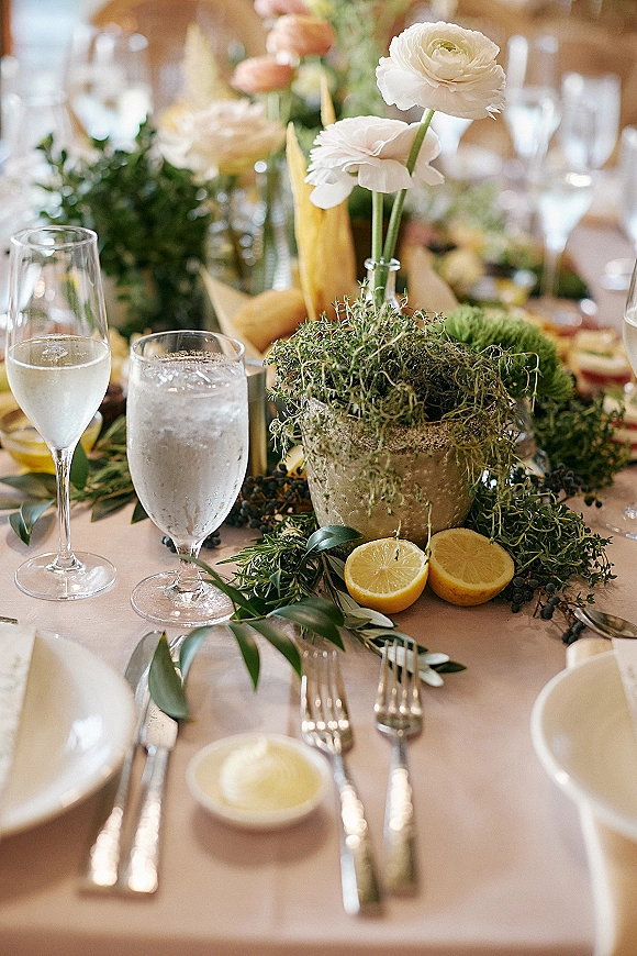 Reception tablescape with wedding table centerpiece of white florals and greenery garland in a ceramic compote vase with lemon halves in soft indoor light