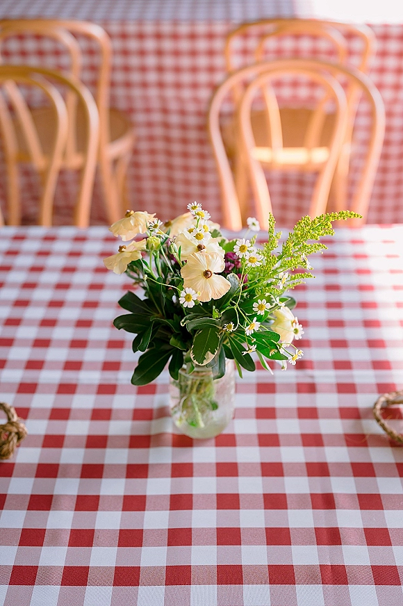 Wedding centerpiece with wildflower wedding centerpiece in a glass jar vase on a red and white gingham tablecloth in a cozy cafe setting