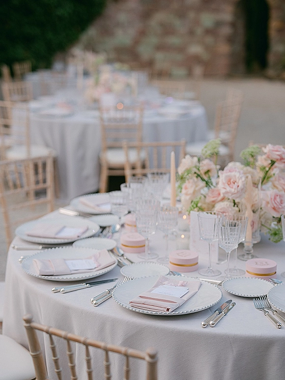 Reception tablescape with a round wedding reception table dressed in white linen, beaded chargers, blush napkins, and taper candles on an outdoor patio