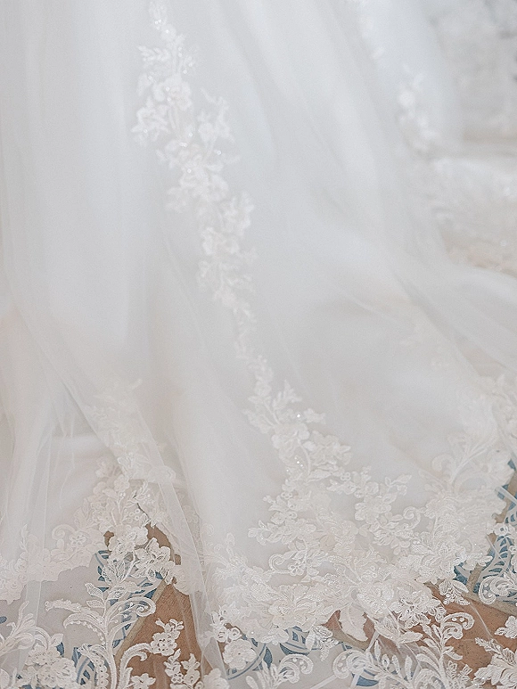 Wedding dress detail with lace wedding dress appliqué, embroidery and beadwork on tulle, laid flat over a patterned rug floor