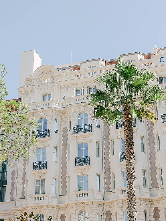 Wedding venue exterior of a luxury wedding venue with wrought iron balconies and tall windows, framed by palm tree greenery and blue sky