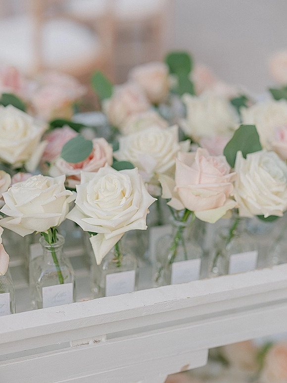 Wedding floral centerpieces with rose bud vase centerpieces, white and blush roses with eucalyptus in labeled glass bottles on a white shelf