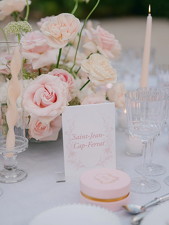 Wedding tablescape with a blush wedding centerpiece, white taper candles in glass holders, menu and place cards on a white cloth outdoors