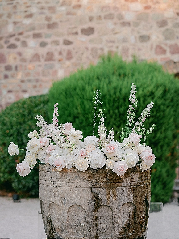 Wedding floral arrangement with fountain floral arrangement of white and blush roses and hydrangeas around a stone basin with water spray, garden hedges behind