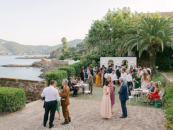 Wedding cocktail hour with outdoor wedding cocktail hour setup of cocktail tables and bistro chairs on a stone terrace overlooking the ocean and mountains