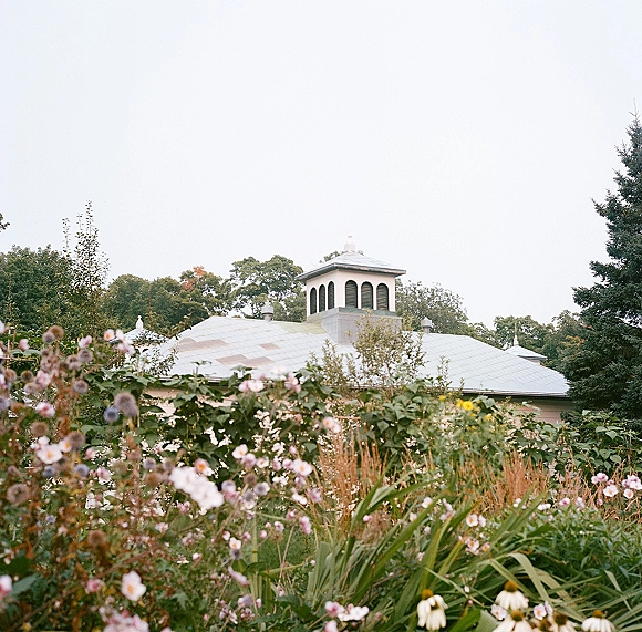 Garden wedding venue with a pavilion building framed by wildflowers and ornamental grasses, surrounded by trees and sky