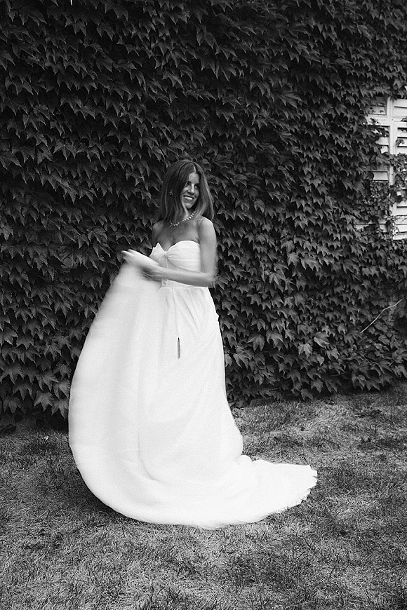 Bridal portrait of a bride in a black and white bridal portrait twirling a strapless wedding dress by an ivy wall and lawn, necklace visible