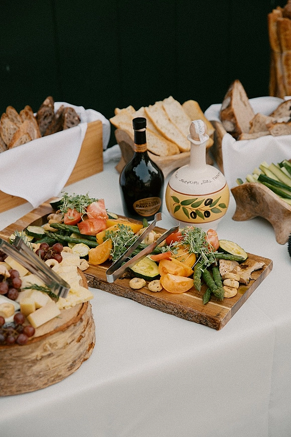 Wedding appetizer spread with cheese, grapes, crackers and sliced bread on rustic wood boards over a white tablecloth, dark wall behind