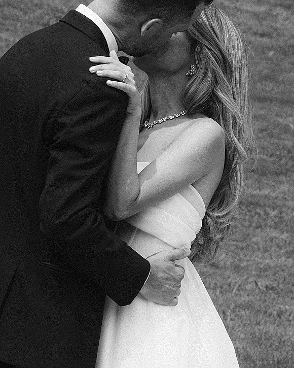 Wedding kiss in a black and white wedding photo, close-up of bride and groom embracing on a grass lawn, engagement ring visible