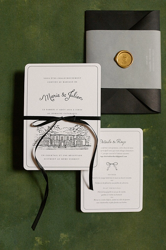 Wedding invitation suite of black and white wedding invitations with black envelope, white belly band and gold wax seal on green fabric backdrop