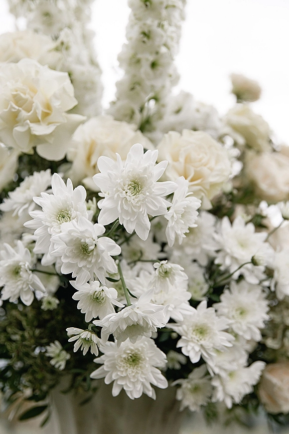 Wedding flowers of white roses and chrysanthemums with greenery accents, photographed close up against a bright sky and blurred florals