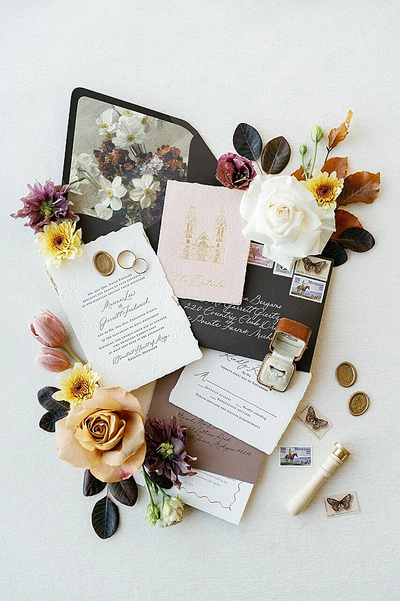 Invitation suite wedding invitation flat lay with calligraphy envelopes, wax seal, stamps, rings and moody floral styling on white surface