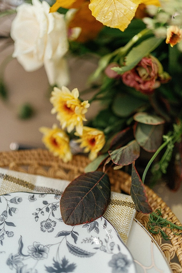 Wedding tablescape with fall wedding tablescape details, layered floral print plates on wicker placemat with eucalyptus and yellow blooms accents