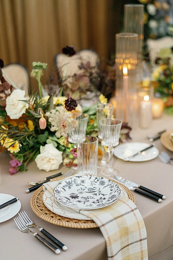 Reception tablescape with a wedding table setting, floral centerpiece and taper candles in glass hurricanes on a banquet table with draped backdrop