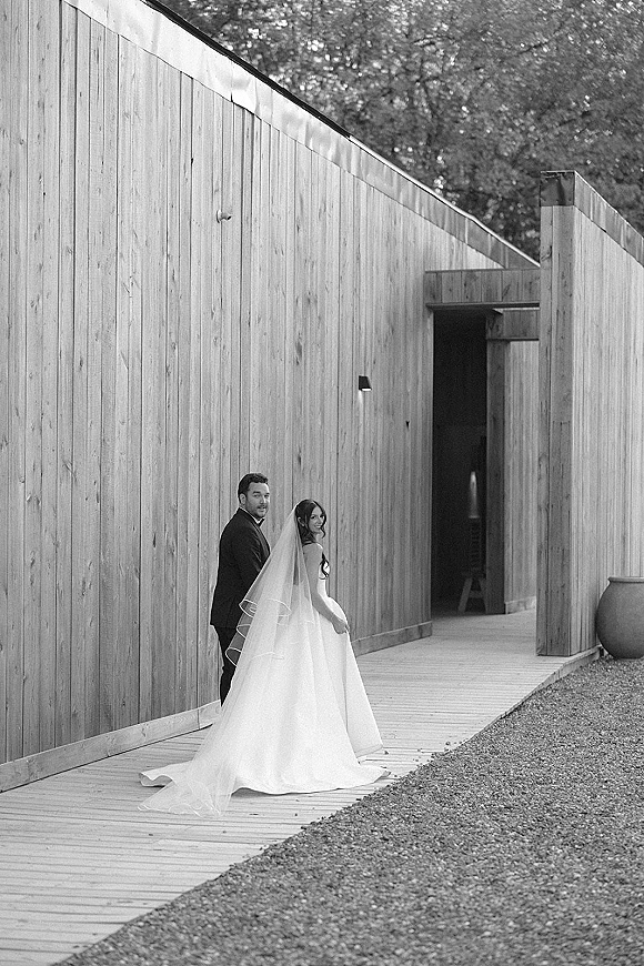 Couple portrait in a black and white wedding portrait, bride and groom looking back with cathedral veil and train by a wood wall