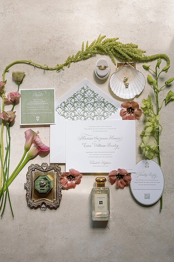 Invitation suite wedding invitation flat lay with sage green cards, patterned envelope, rings and pearl earrings on neutral stone surface