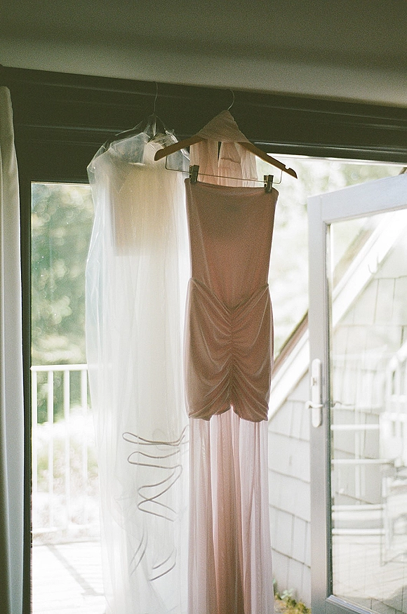Bridesmaid dress in blush bridesmaid dress shade with tulle overlay, hanging on a hanger by window light near an open glass door