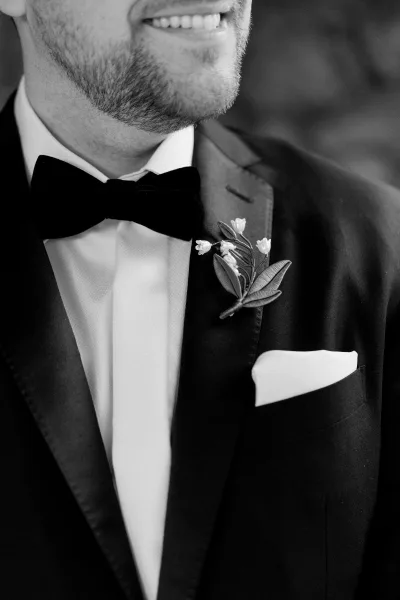 Groom details of a black tie groom, highlighting a tailored tuxedo and a fresh boutonniere pinned neatly to his jacket.