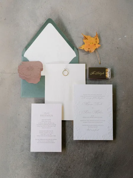 Invitation suite featuring an embossed floral invitation, styled with an autumn leaf on a concrete surface for a refined, minimal look