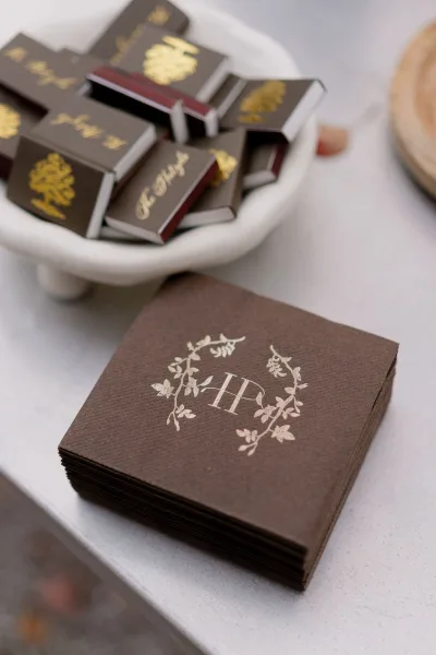 Custom cocktail napkins styled as monogram wedding napkins with gold foil, neatly stacked on a wooden tray.