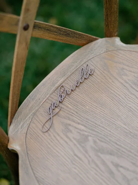 Wedding place card as a laser cut name sign, attached to a wood chair on a grass lawn for an elegant outdoor display.