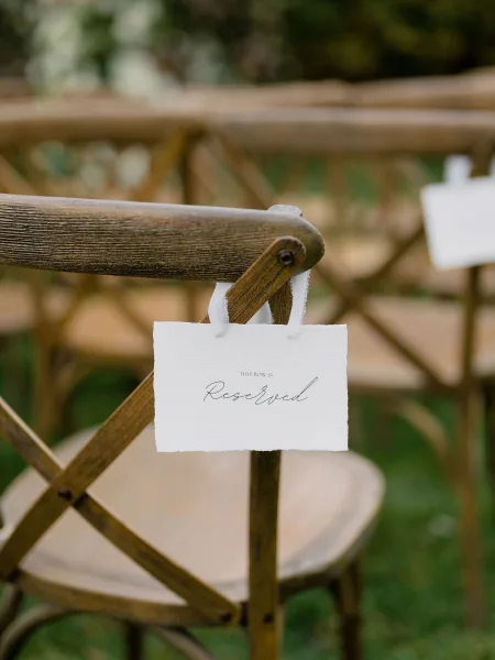 Wedding reserved sign, a ceremony chair sign tied with a ribbon, set on a grass lawn among garden greenery for an outdoor seating row