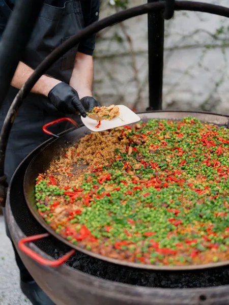 Paella station for wedding paella catering, a paella pan ready by a stone wall with climbing greenery over a gravel courtyard.