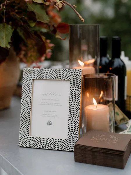 Signature cocktail sign for the wedding bar menu in a patterned frame, set on a bar countertop with garden greenery in the background.