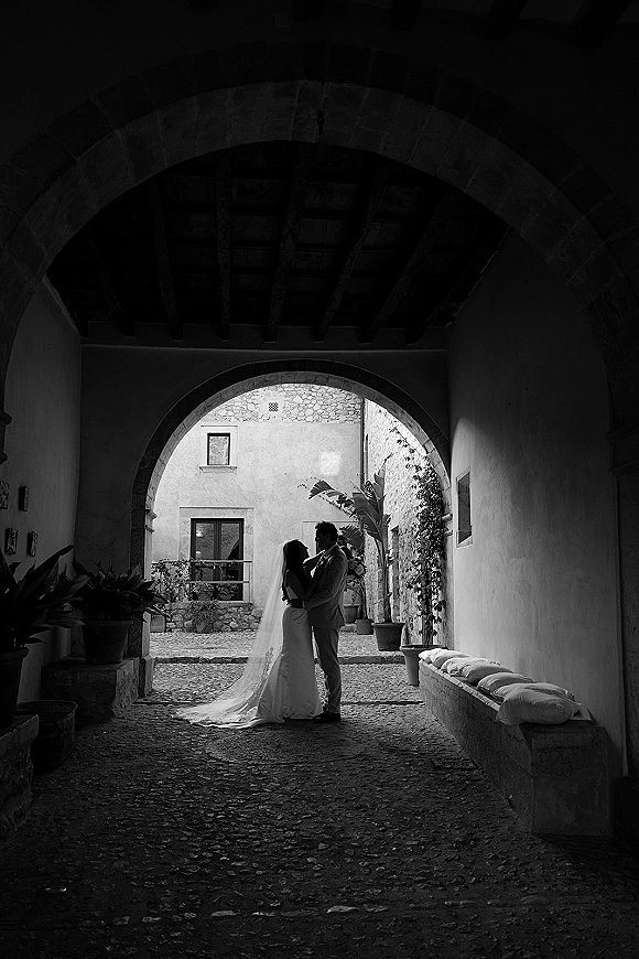 Couple portrait in a black and white wedding portrait, bride and groom embracing under a stone archway in a cobblestone courtyard