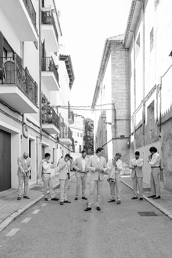 Groomsmen portrait of men in tan suits wearing sunglasses, standing on a narrow city street with stone buildings and balconies