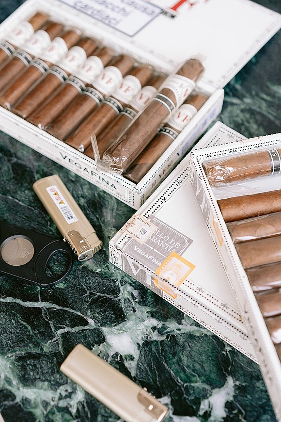 Wedding cigar bar with cigar boxes and cigars beside a cutter on a green marble tabletop, styled as a cigar bar wedding setup