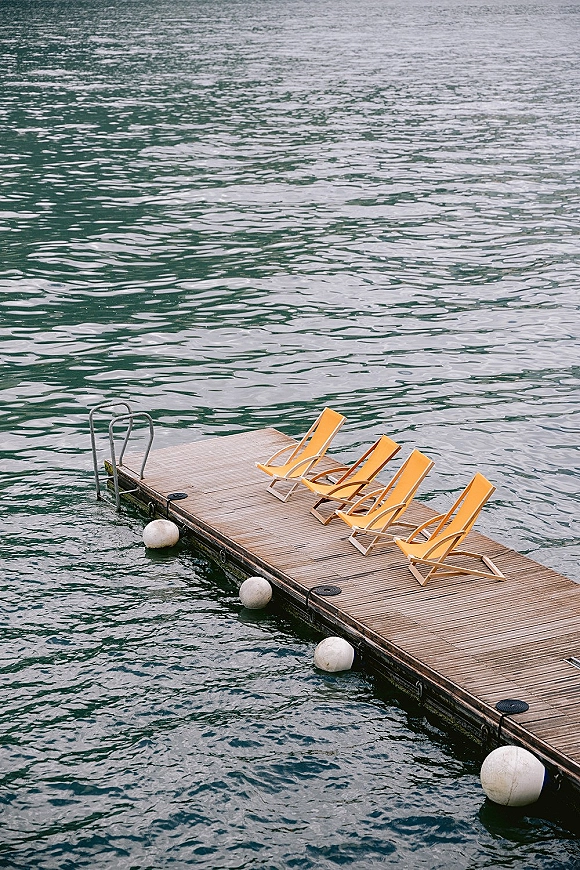 Lakeside dock with dock lounge chairs, bright yellow deck chairs and ladder beside buoy floats over rippling lake water