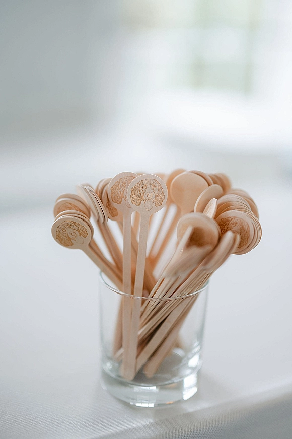 Wedding drink stirrers, custom drink stirrers engraved on wood and resting in a clear tumbler on a white tablecloth in bright window light