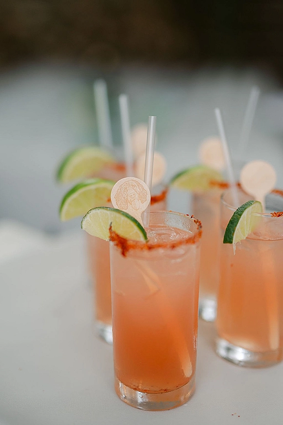 Wedding signature drinks in cocktail glasses with lime wedges and chili-salt rims, served over ice with clear straws on a white tabletop