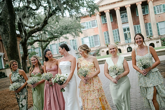 Bridesmaids photo of a bride with bridesmaids holding baby’s breath bouquets in a brick courtyard beside a historic mansion with columns