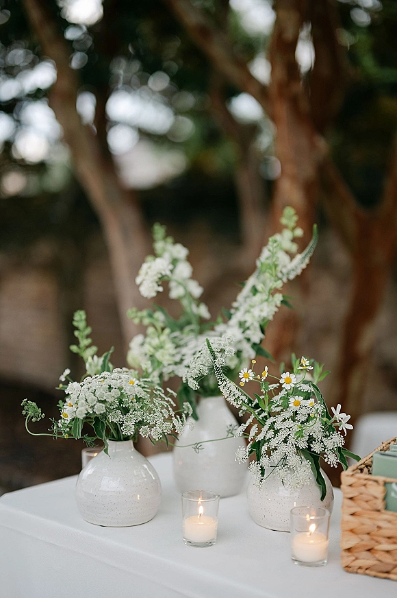 Wedding table florals with bud vase centerpiece in white ceramic vases, wildflowers and votive candles on a garden table with bokeh lights
