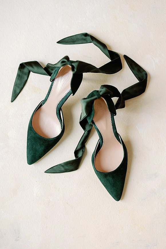 Bridal shoes in emerald green with pointed toes and ankle-wrap satin ribbon ties, arranged in a flat lay on a white surface