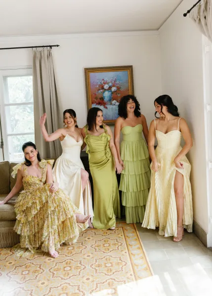 Bridesmaids portrait with mix and match bridesmaid dresses, the women laughing in varied ruffles in a room with a sofa and patterned rug