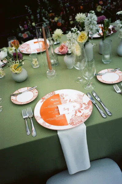 Wedding place setting for reception table decor featuring a patterned dinner plate, framed by garden flowers in the background.