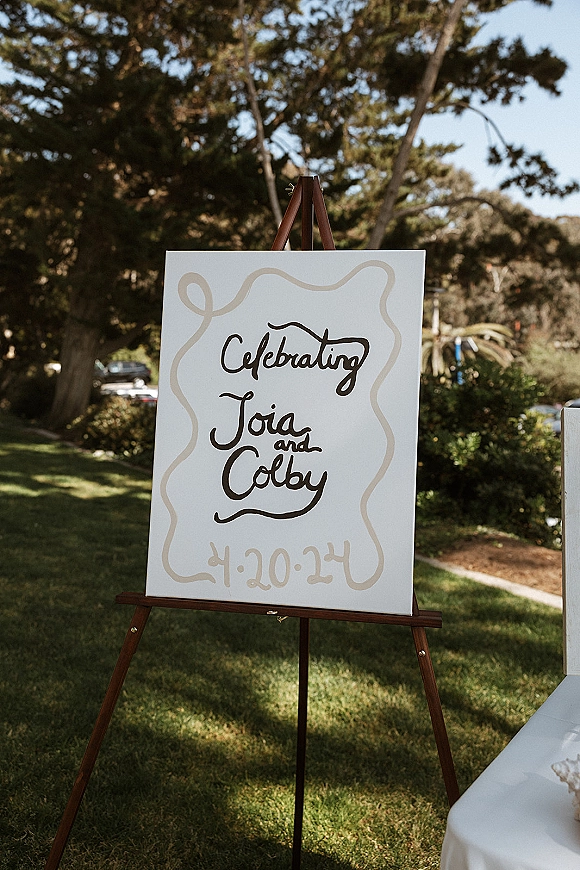 Wedding welcome sign, hand painted wedding sign on a wood easel with calligraphy lettering set on a grassy lawn with trees in daylight