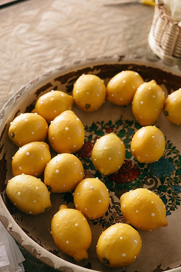 Lemon wedding decor arranged as a lemon centerpiece idea on a ceramic platter with pearl pins, set on a tablecloth beside a wicker basket