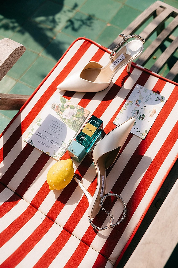 Bridal shoes flatlay with wedding shoe detail of white pointed toe heels and crystal ankle straps on a green-tiled pool deck