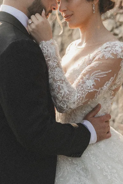 Wedding couple portrait, close up wedding portrait of bride and groom embracing, her lace long sleeves and ring catching sunlight by trees