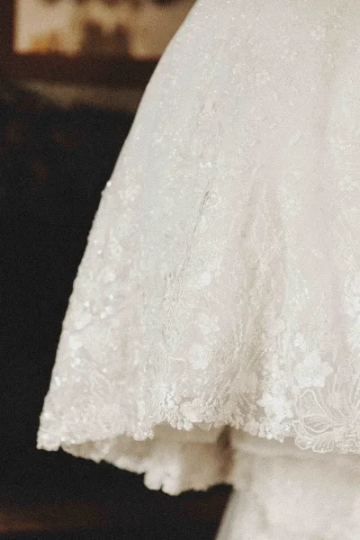 Wedding dress detail with lace wedding dress beading and embroidery along a scalloped hem, falling onto a dark carpeted interior floor