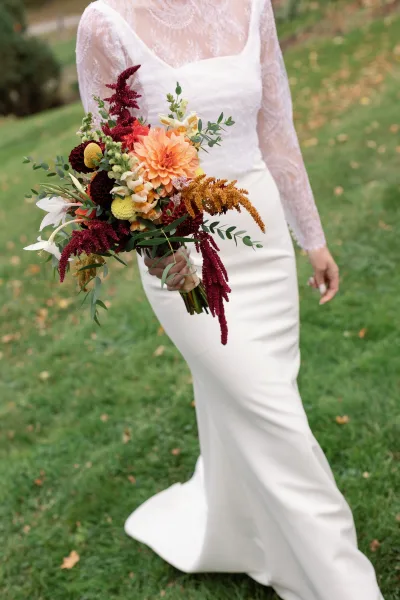 Bridal bouquet in a fall wedding bouquet style with dahlias, lilies, burgundy and yellow blooms, held over a lawn with fallen leaves