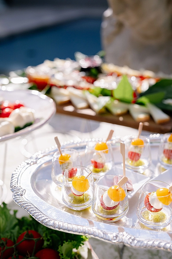 Wedding cocktail hour appetizers on a wedding passed appetizers tray with mini caprese cups, wooden picks, and basil on a buffet table
