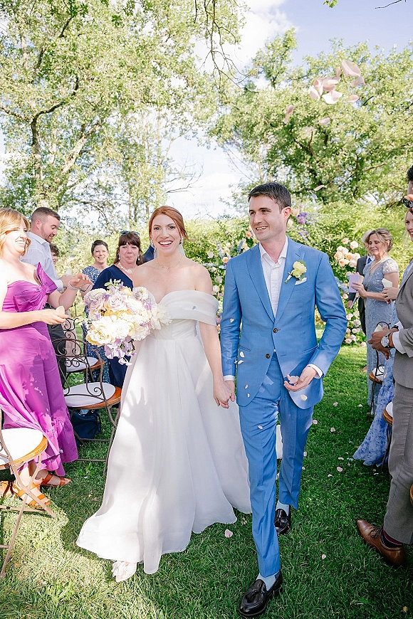 Wedding recessional as bride and groom walk the aisle hand in hand while guests toss flower petals in a sunny garden ceremony setting