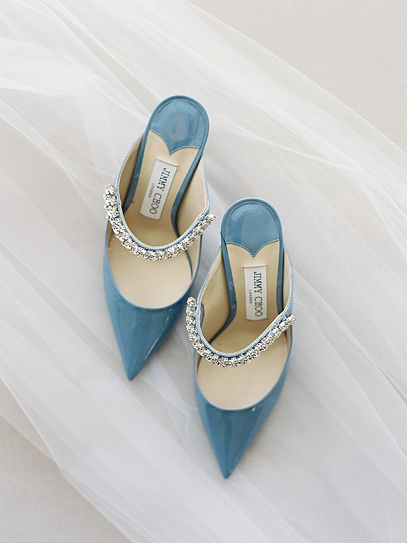 Bridal shoes in blue satin mules with rhinestone strap and pointed toe resting on airy white tulle fabric for a something blue detail shot